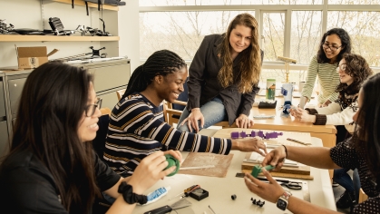 Women biomedical engineering students working at a table on projects alongside woman faculty member with long hair, blazer and jeans.
